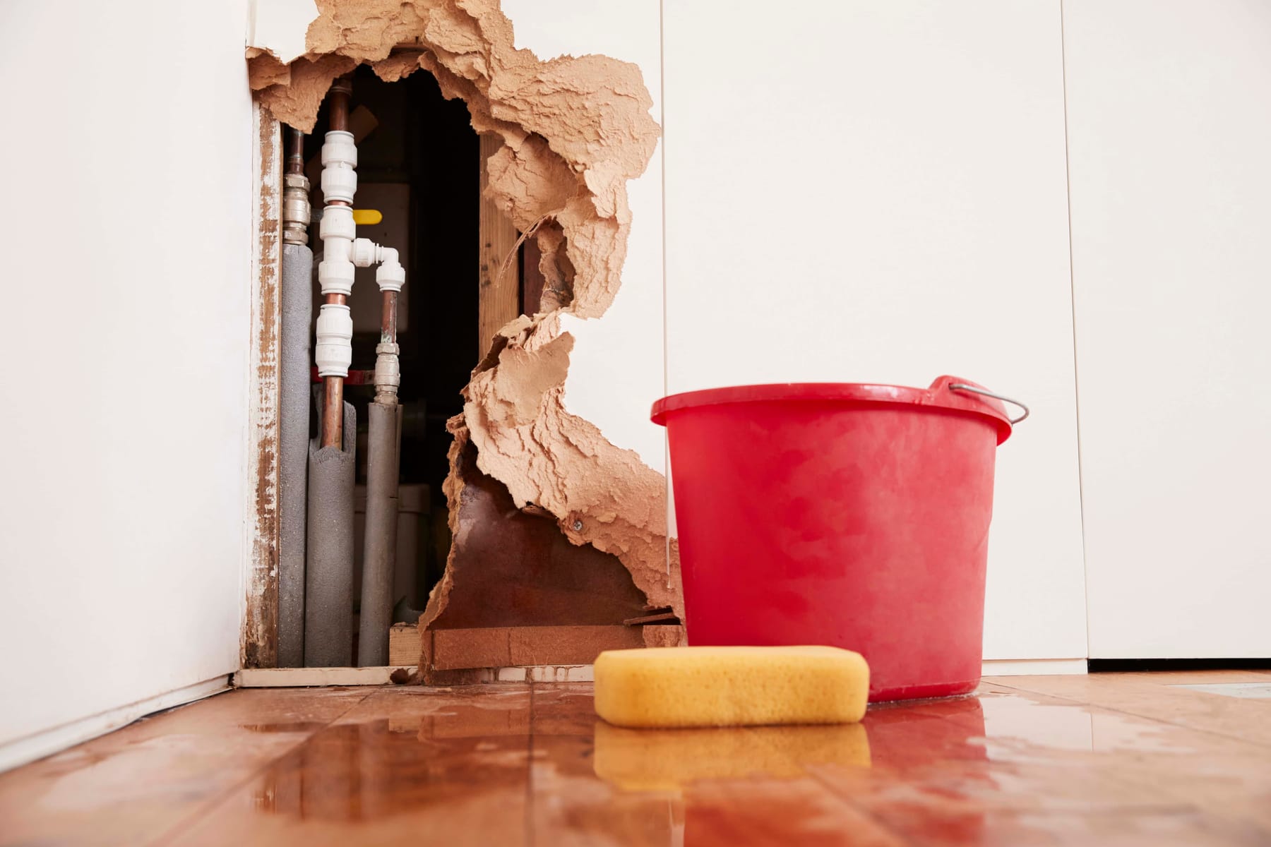 Burst water pipes behind a damaged wall